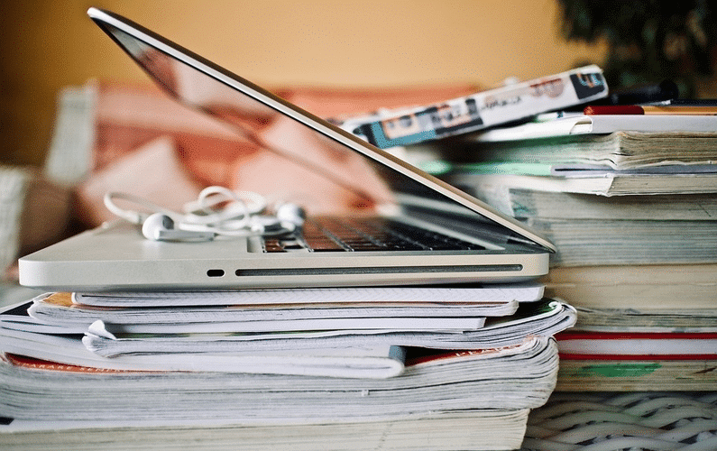 laptop on pile of magazines | online teaching jobs | Peace Evolution