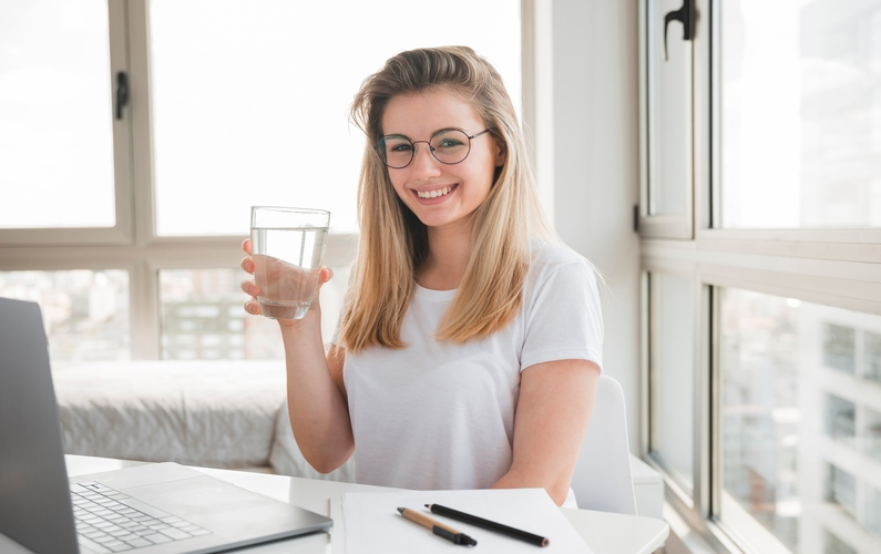 girl sitting at a desk holding a glass of water | practicing fasting | Peace Evolution