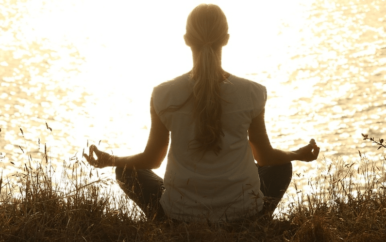 girl sitting next to a lake meditating | practice water fasting | Peace Evolution