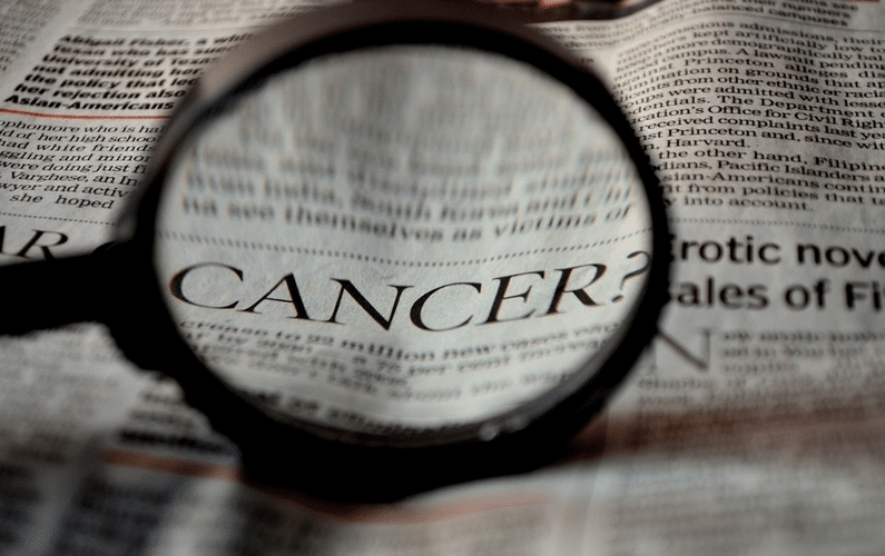 newspaper with magnifying glass highlighting the word cancer | health problems | Peace Evolution