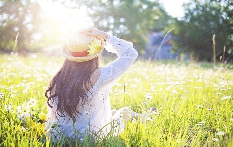 young woman with straw hat sitting in field of flowers | healthy eating | Peace Evolution